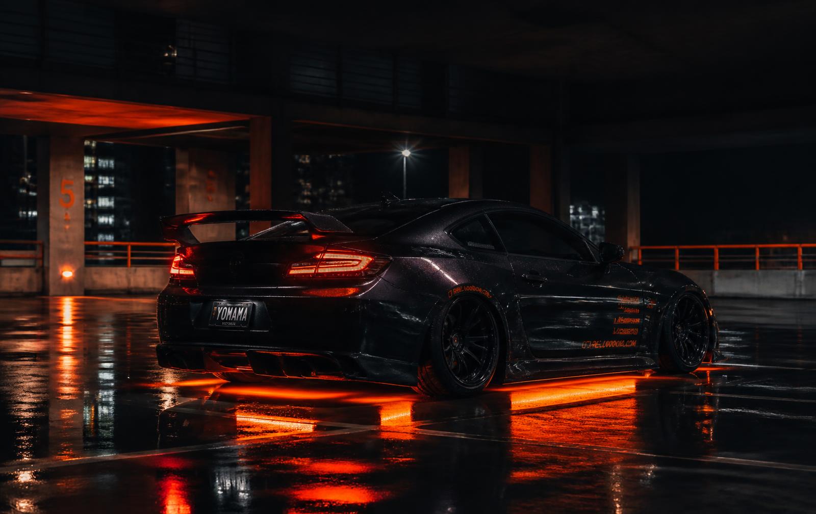 Custom blacked-out coupe with orange underglow in a night parking garage